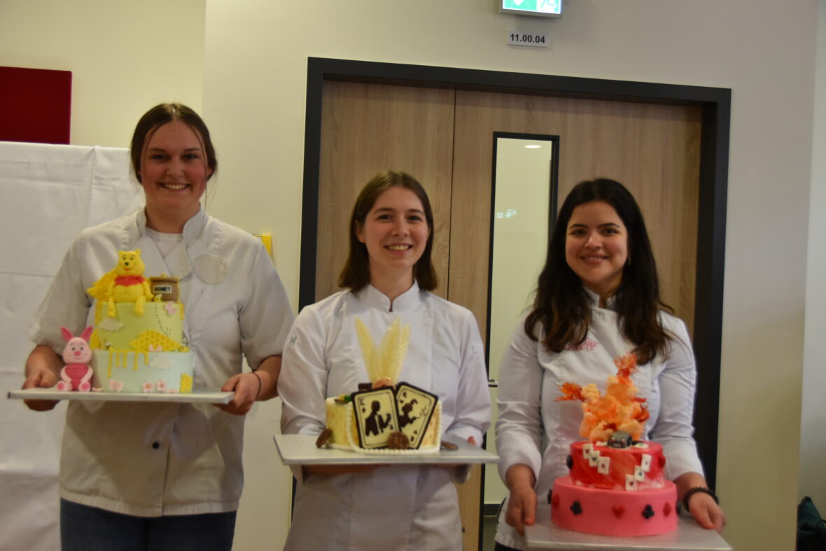 Drei junge Frauen halten jeweils einen sehr individuell gestalteten Kuchen in den Händen