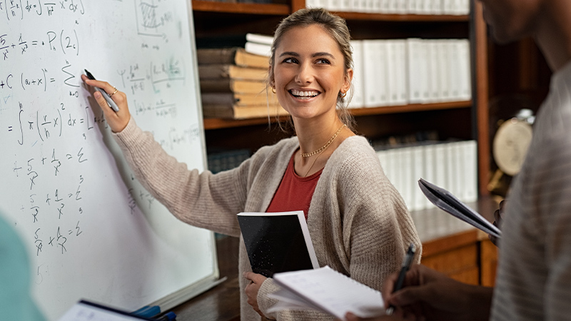 Junge Frau mit Stift in der Hand vor Tafel mit mathematischen Formeln